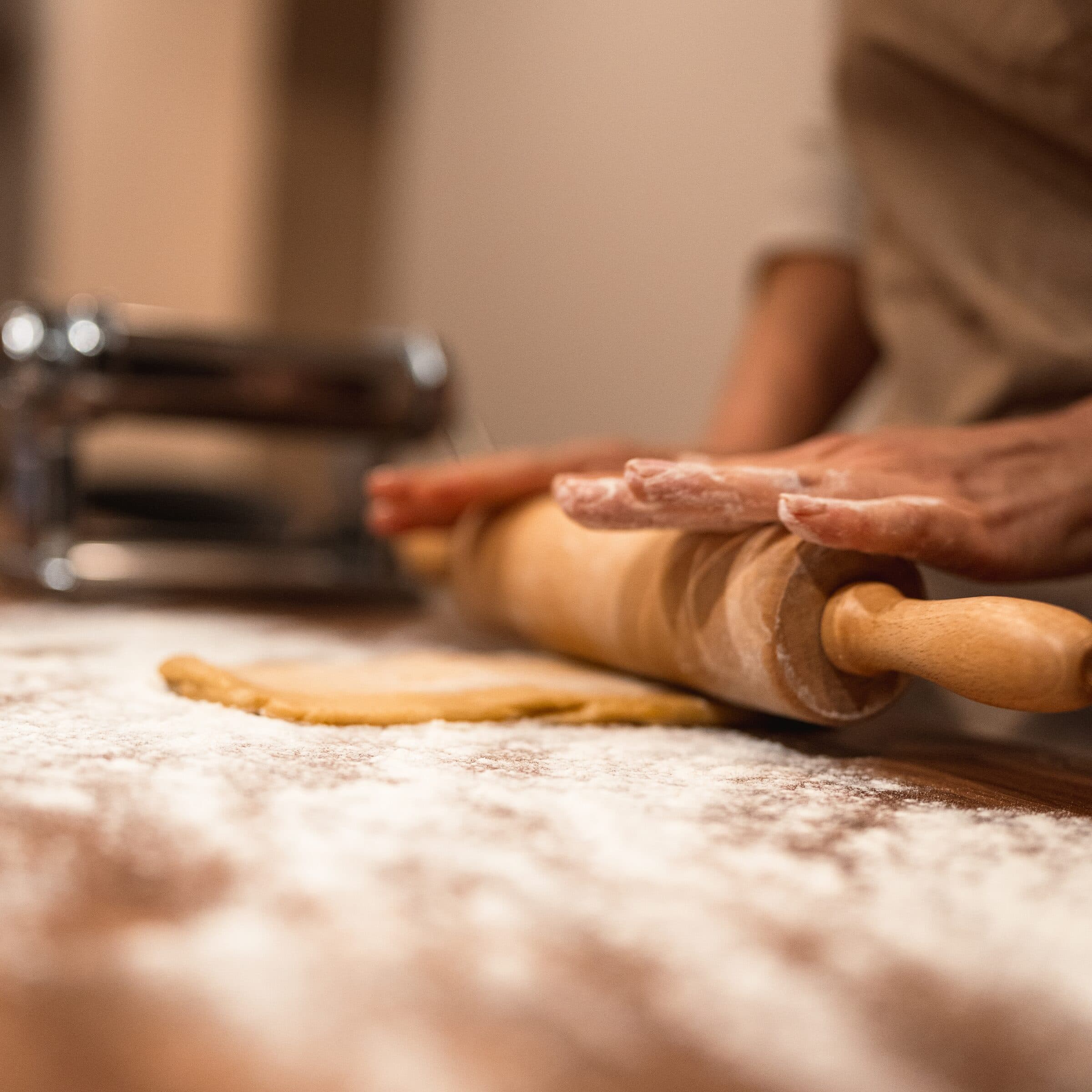 Des mains farinées étalent la pasta au rouleau, sur la table couverte de farine
